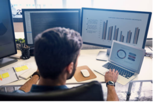 Man at a desk with multiple monitors conducting research on college programs.