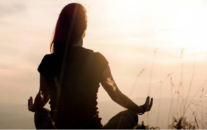 Woman meditating in a yoga pose outdoors during a bright sunset.